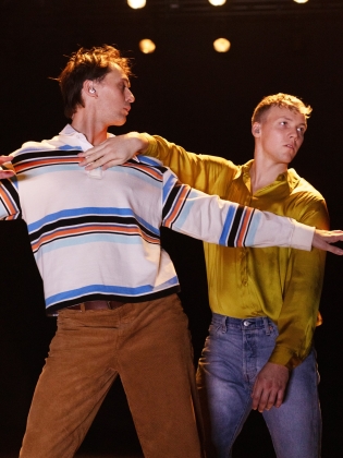 Två unga män dansar på scen, en i randig tröja och manchesterbyxor, den andre i gul skjorta och jeans.