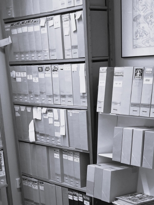 Arkivrum med hyllor fyllda av märkta tidskriftssamlare och pärmar i flera rader.